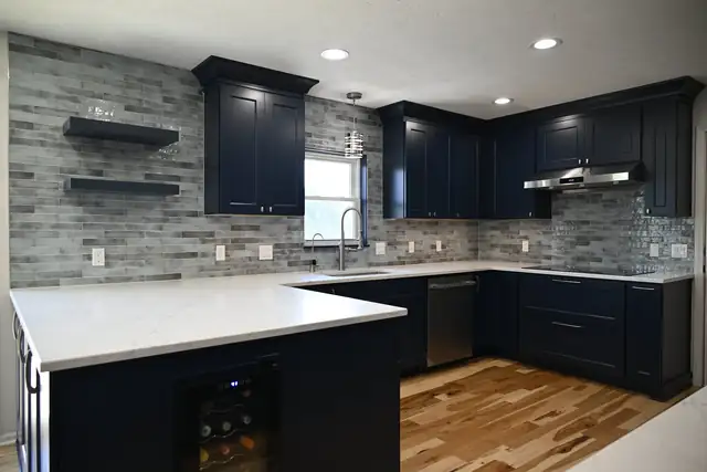 Kitchen by Wright's Renovations with navy shaker cabinets, a white quartz waterfall peninsula, gray brick-look backsplash and floating shelves