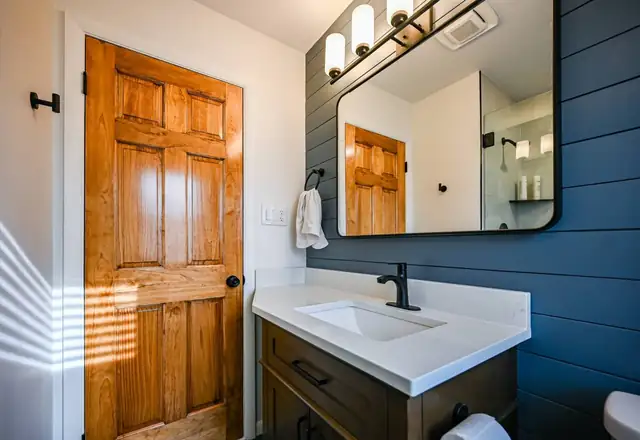 Basement bathroom remodel with navy shiplap wall, black fixtures, white vanity top and natural wood door