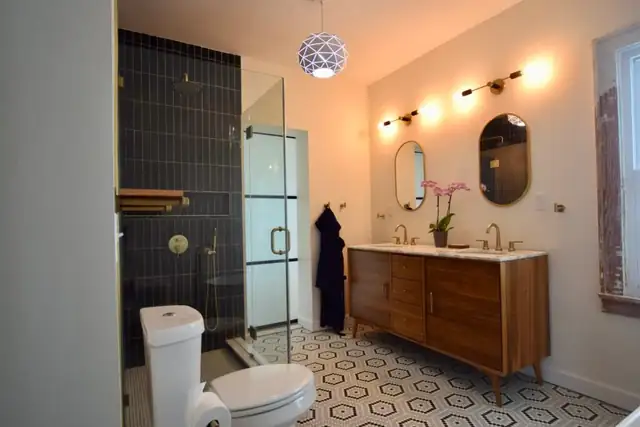 Bathroom remodel with dark vertical tile shower, wood vanity, two round mirrors and patterned tile floor