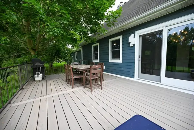 Composite deck and patio with outdoor dining set beside a navy blue sided house