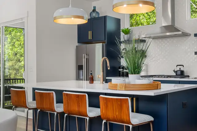 Remodeled kitchen with navy island, white quartz top, wood and leather stools, brass faucet and a single pendant light