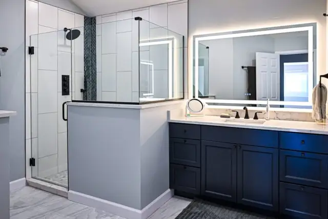 Plymouth Township, MI primary bathroom with frameless glass shower, backlit mirror and navy vanity