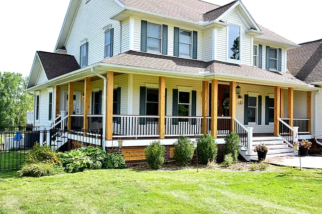 White farmhouse with a wraparound covered porch, new wood columns, white railings and front steps